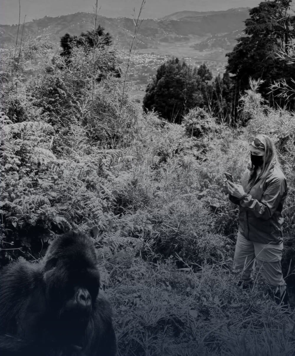 Kate Whelan standing quietly near a mountain gorilla in the forests of Rwanda, in black and white.