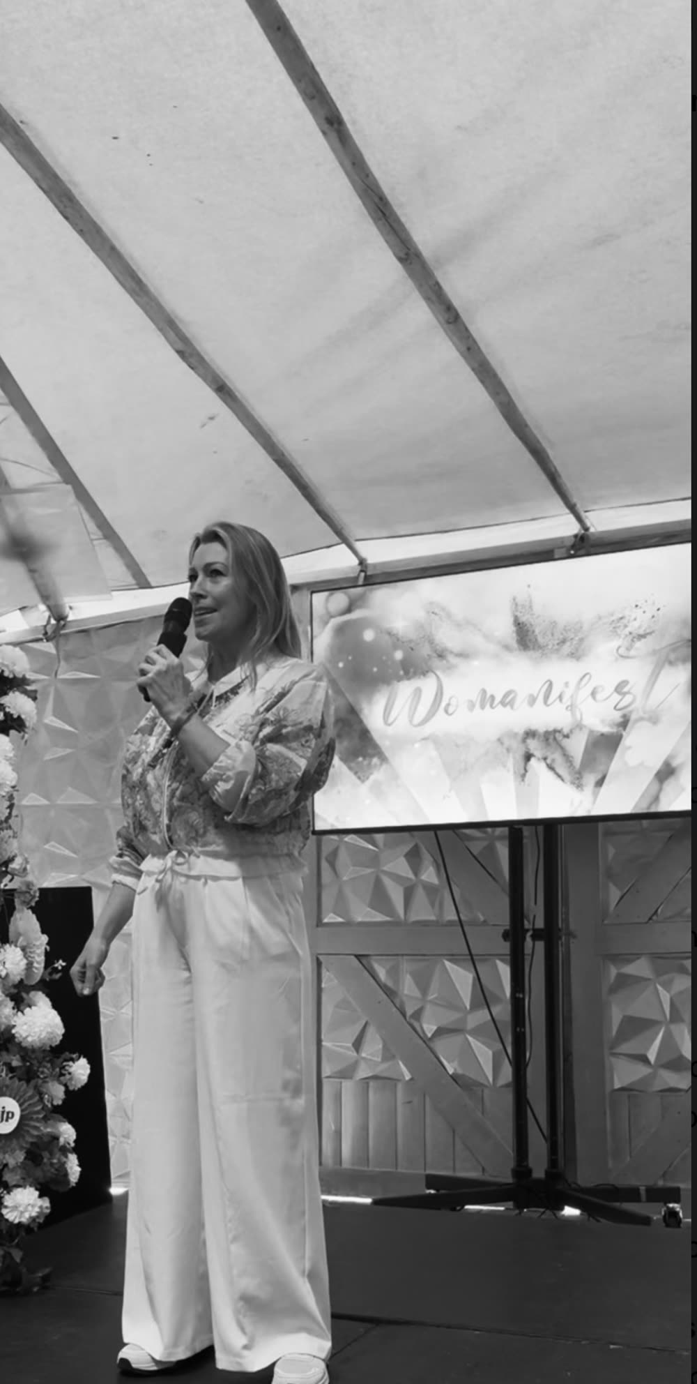 Kate Whelan on stage with a microphone, addressing an audience, in black and white.